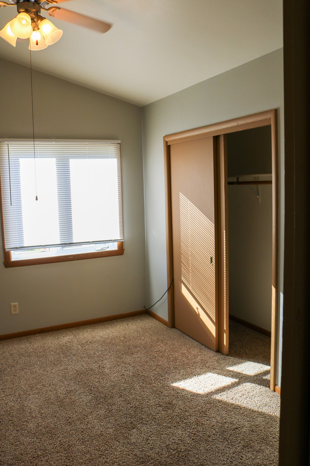A room with a ceiling fan and a window with blinds.