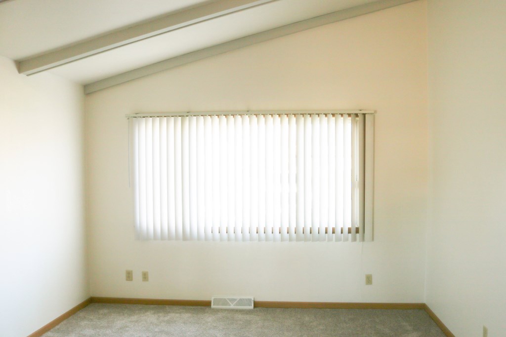 A room with a window covered by white blinds.