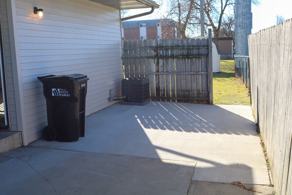 A black trash can sits on a concrete patio.