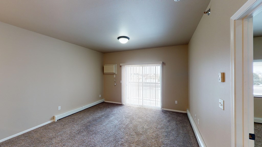 A spacious room with a carpeted floor and a window with blinds.