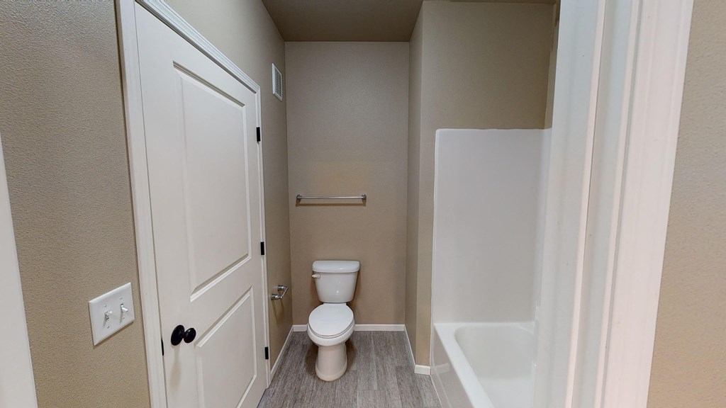 A white toilet is in a small bathroom with a white door and a white sink.