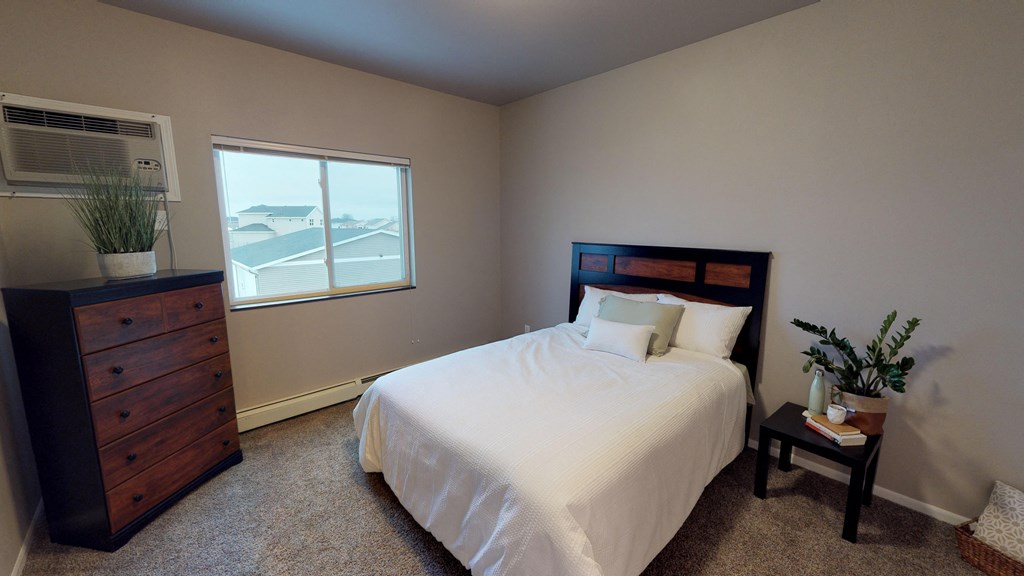 A bedroom with a large bed, a nightstand, and a window overlooking the street.