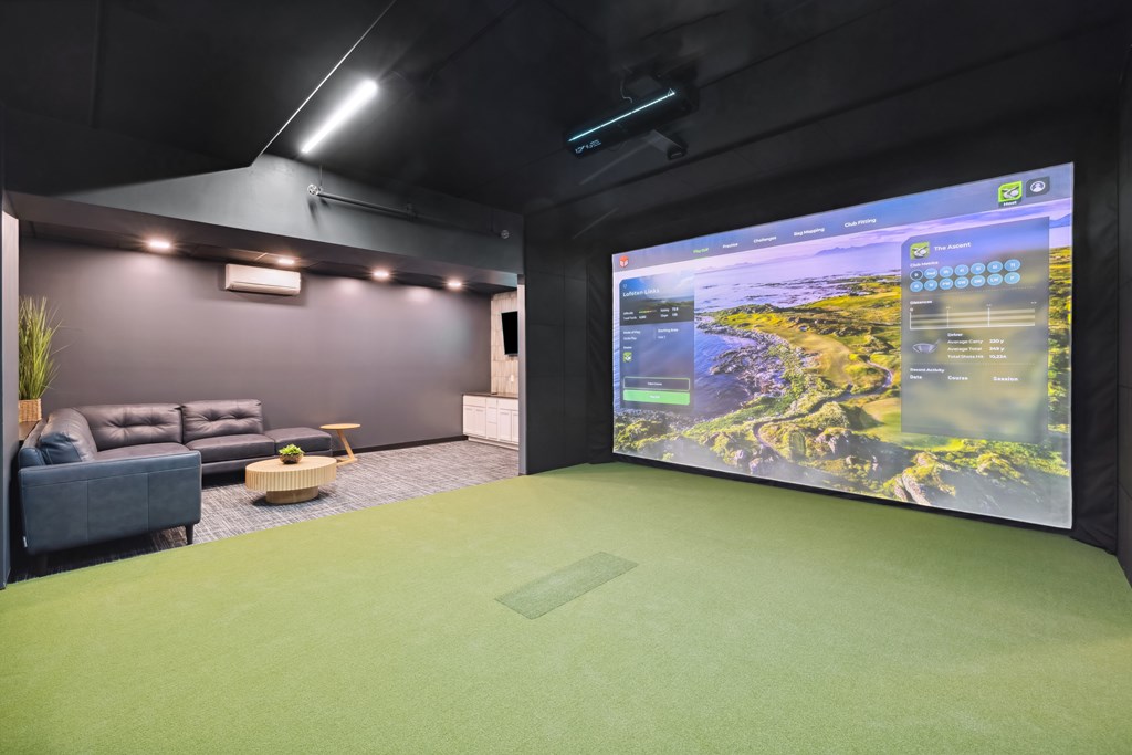 A golf simulator room with a large screen on the wall and a couch.