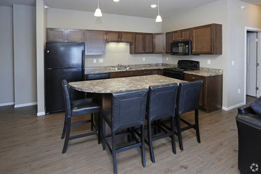 a kitchen with an island with four chairs and a black refrigerator