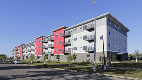 A street view of a multi-story building with red and grey sections.