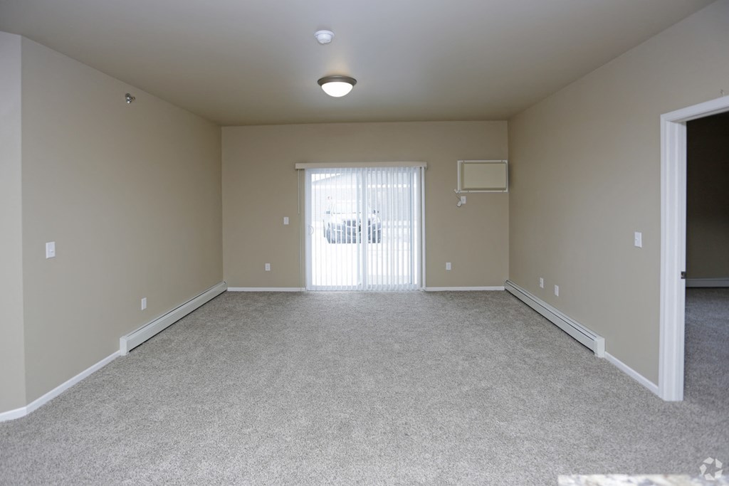 A spacious room with a carpeted floor and a window with blinds.