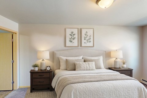 A bedroom with a large bed, two nightstands with lamps, and two framed pictures on the wall.