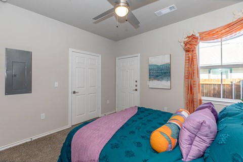 A bedroom with a bed covered in a teal and pink comforter and two orange and purple pillows.