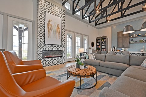 A living room with a grey couch, orange chairs and a patterned wall hanging.