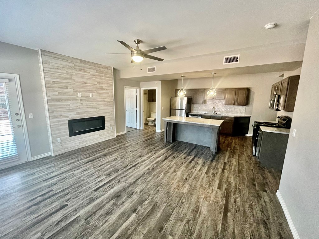 an empty living room with a fireplace and a kitchen