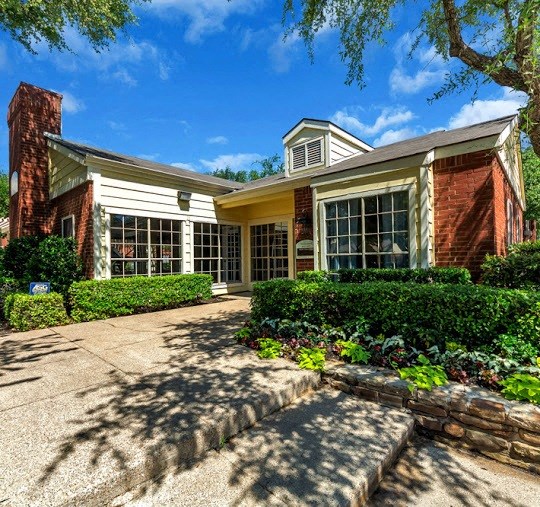 the front of a brick house with a driveway and trees