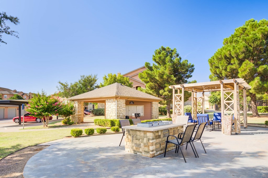 A patio with a table and chairs is surrounded by a stone wall and trees.