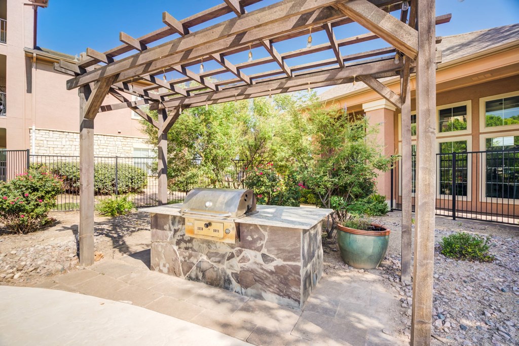 A wooden pergola is over a stone bench with a planter underneath.