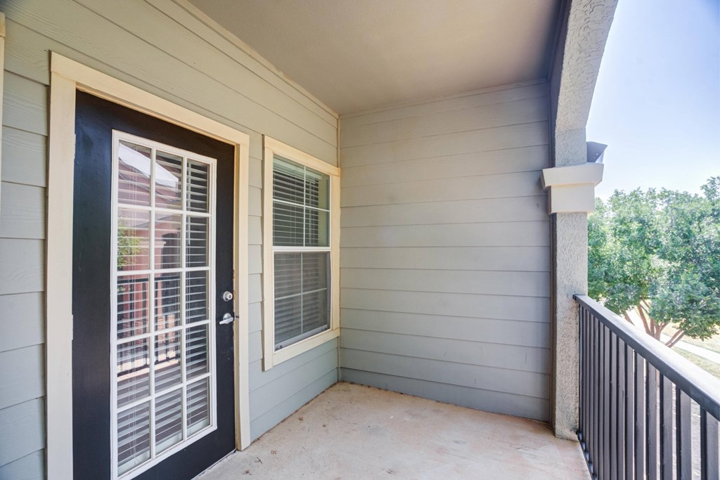 A balcony with a black door and a window with white blinds.