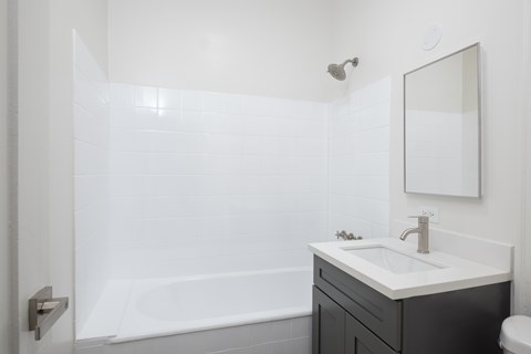 A white bathroom with a black vanity and a white tub at Westmore Manor Apartments, Los Angeles, California