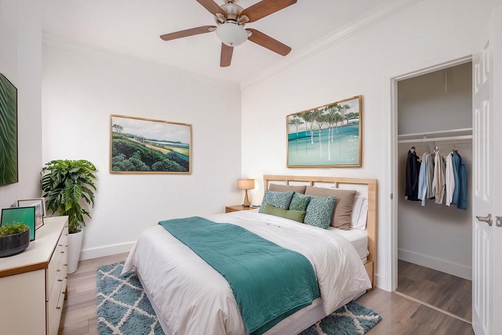 A bedroom with a bed, a ceiling fan, and a painting of a beach scene.