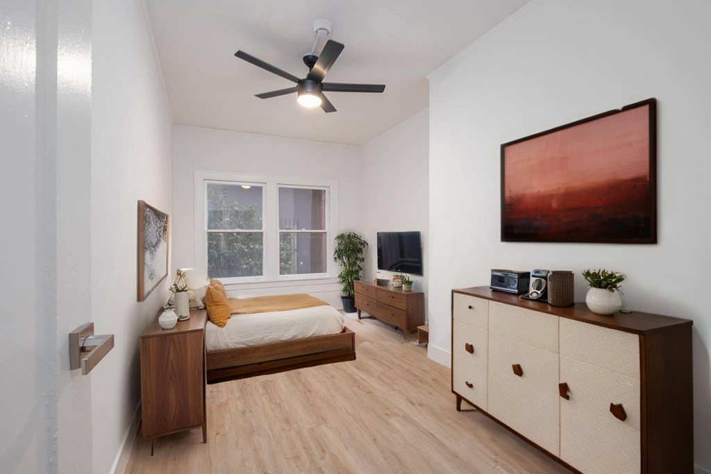 A bedroom with a bed, dresser, and a ceiling fan.