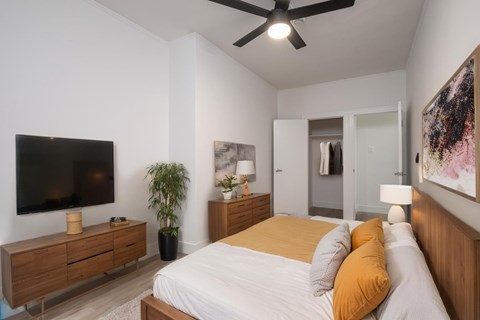 A bedroom with a bed, a television, and a ceiling fan.