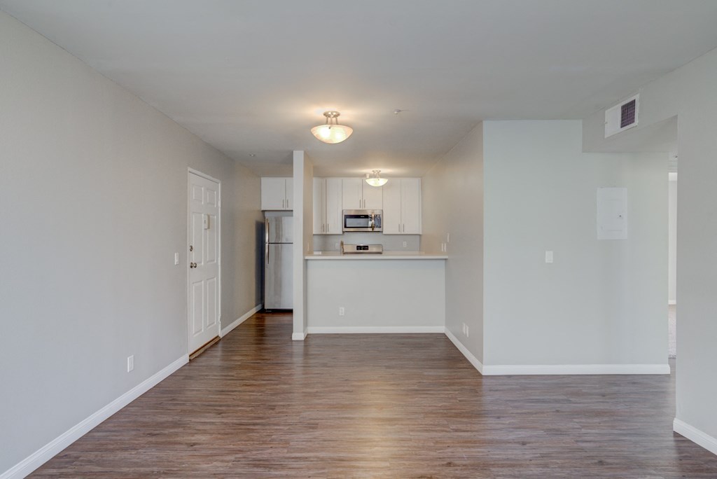 an empty living room and kitchen with white walls and wood flooring