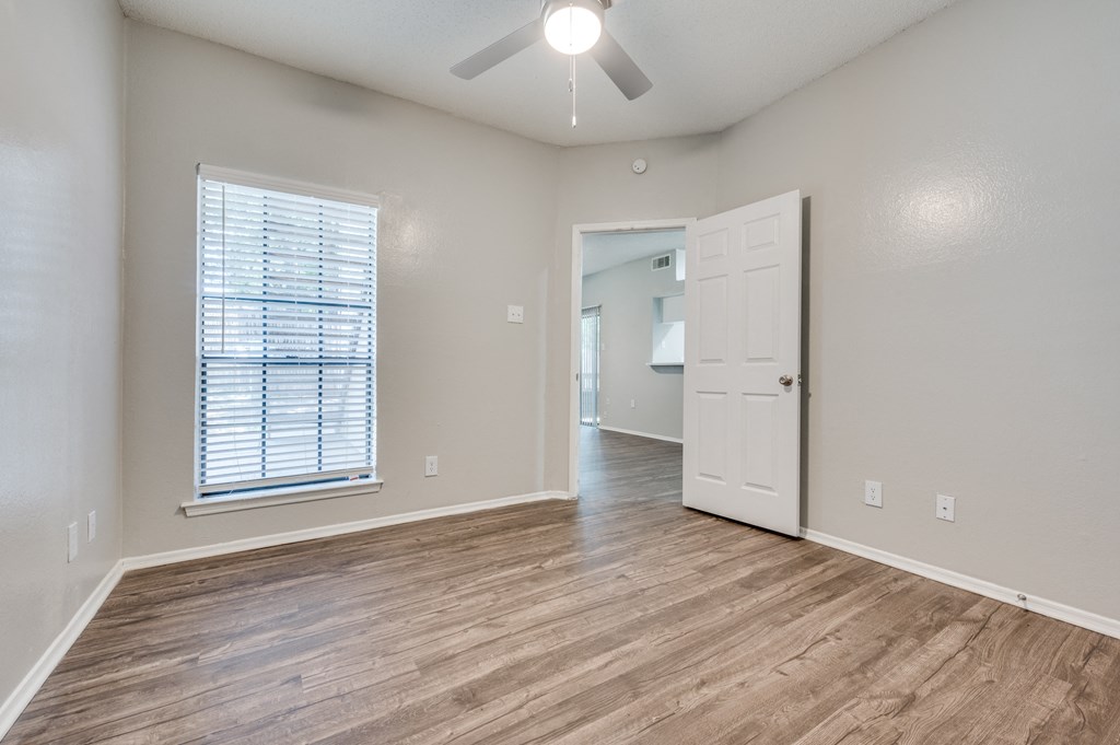 an empty living room with a white door and a ceiling fan