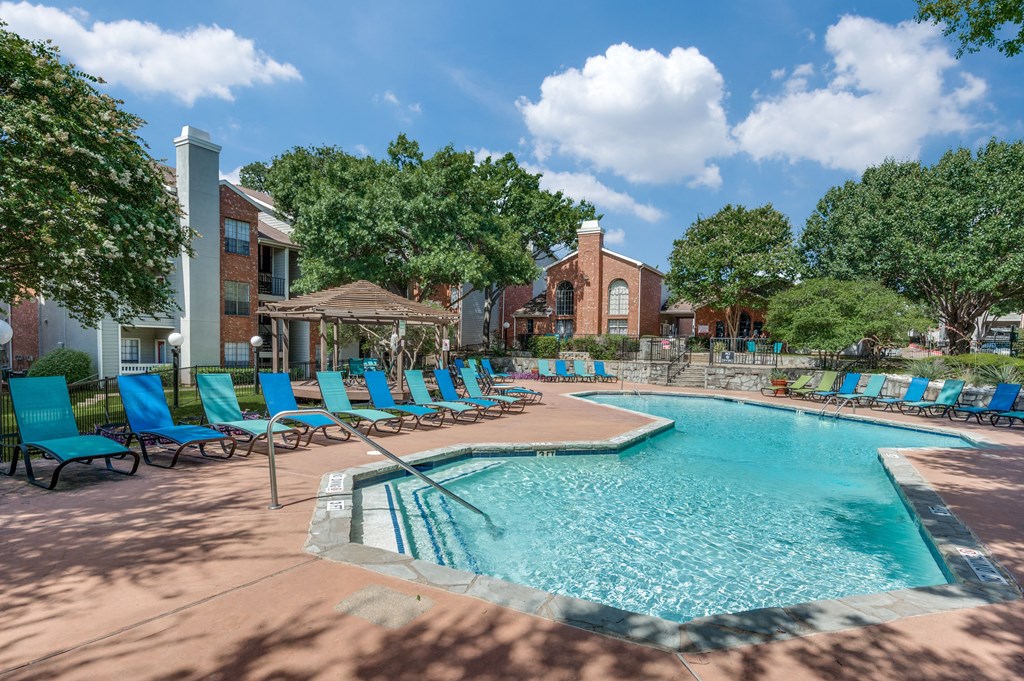 a resort style swimming pool with blue chairs and a building in the background