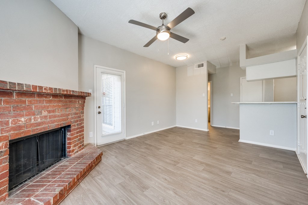 an empty living room with a brick fireplace and a ceiling fan