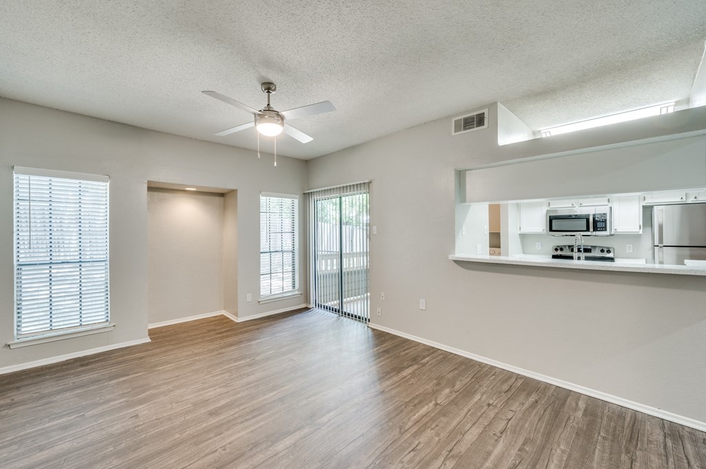 an empty living room with a ceiling fan and a kitchen