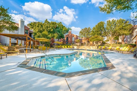 A large outdoor swimming pool surrounded by trees and a building in the background.