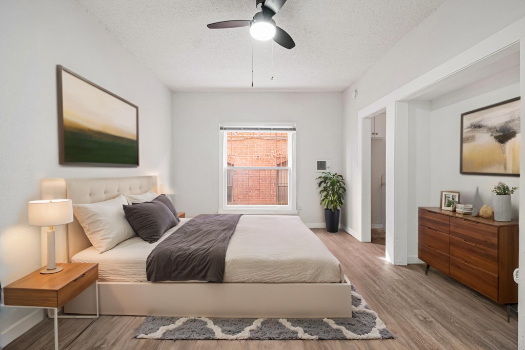 A bedroom with a large bed, a ceiling fan, and a window with a view of a red building at Hillstone Flats Apartments, Los Angeles, 90004