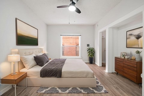 A bedroom with a large bed, a ceiling fan, and a window with a view of a red building.