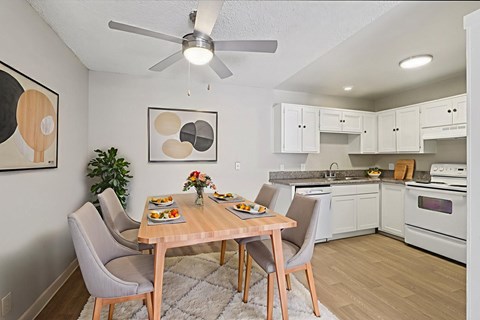 A dining room with a table set for two and a plant in the corner.