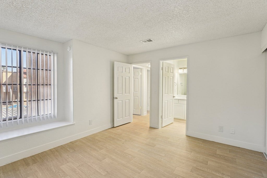 A room with white walls and wooden flooring, with two doors open.