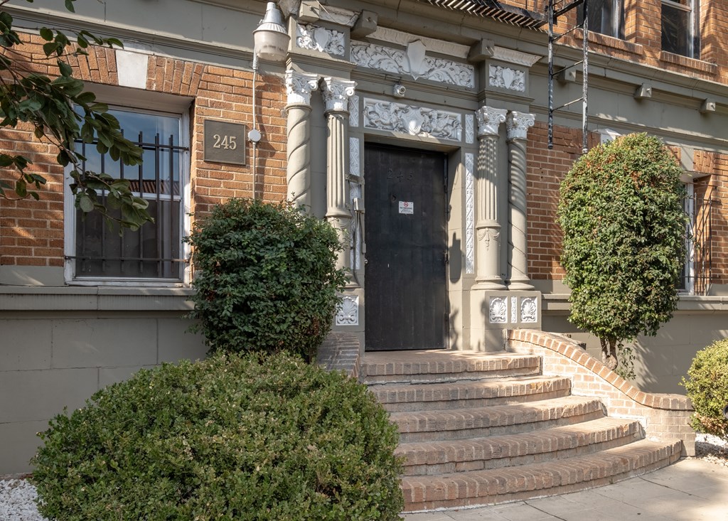 A black door is flanked by two bushes and a set of steps at Kenmore Park Apartments, Los Angeles, CA, 90004