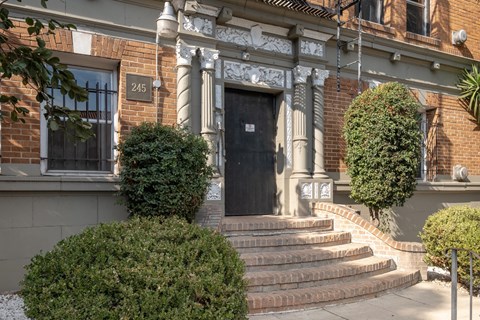 A black door is flanked by two topiary bushes at Kenmore Park Apartments, California