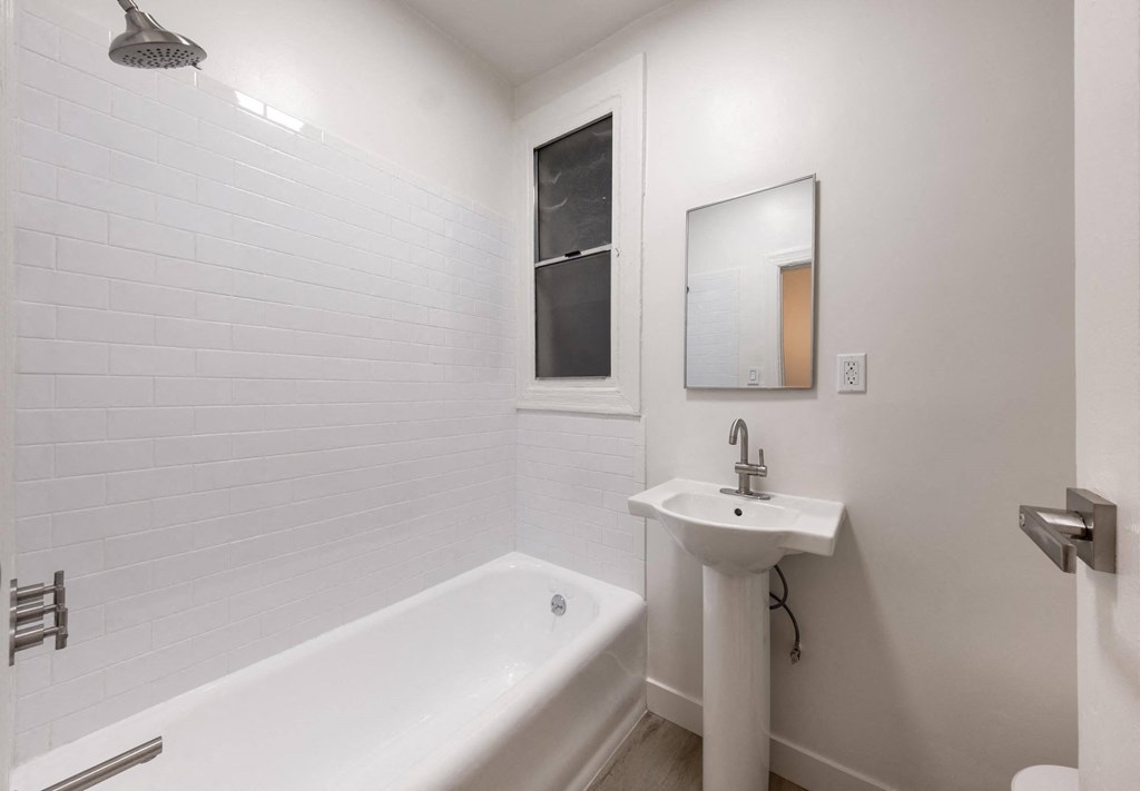 A white bathroom with a tub, sink, and mirror at Kenmore Park Apartments, Los Angeles, 90004