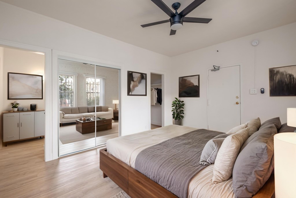A bedroom with a bed, a ceiling fan, and a mirrored doorway leading to a living room. A bedroom with a bed, a ceiling fan, and a mirrored doorway leading to a living room at Kenmore Park Apartments, Los Angeles, 90004