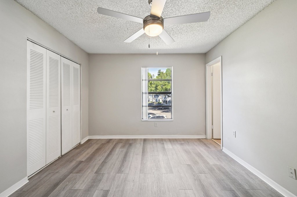 A room with a ceiling fan and a window showing a view of trees and buildings outside.