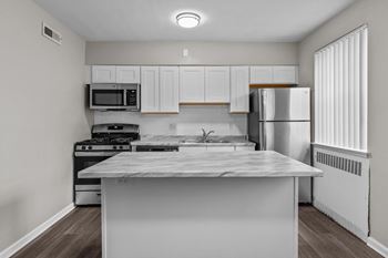 an empty kitchen with white cabinets and stainless steel appliances and a marble counter top