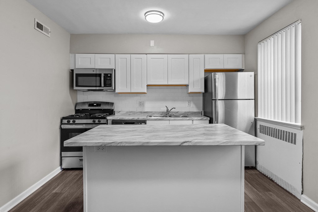 an empty kitchen with white cabinets and stainless steel appliances and a marble counter top