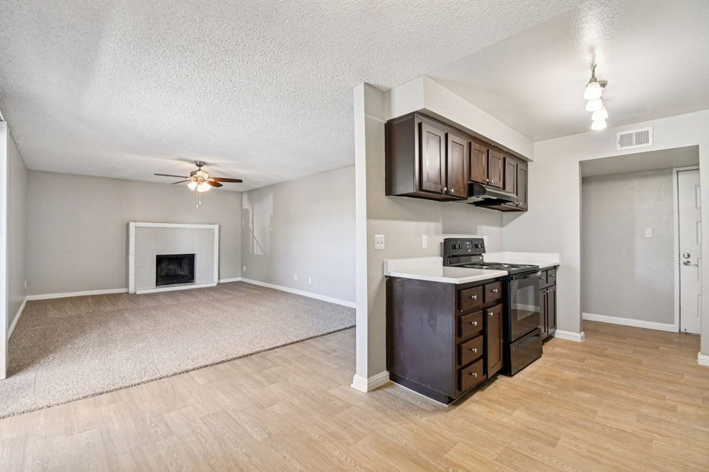 A living room with a fireplace and a kitchen area with brown cabinets.
