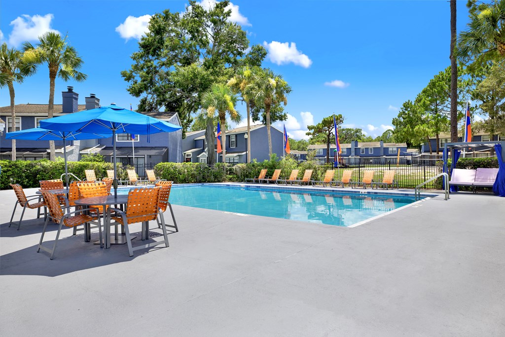 A pool area with a table and chairs and a blue umbrella.