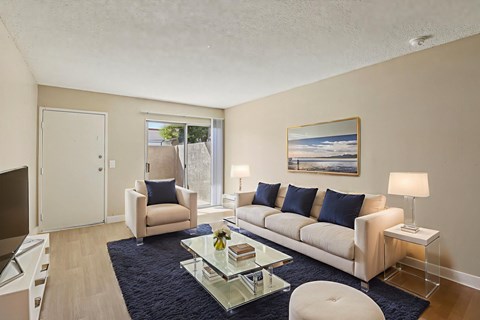A living room with a white couch, a glass coffee table, and a painting on the wall.