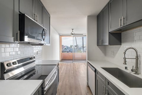 A modern kitchen with a stove top oven, microwave, and a sink.at Menlo Terrace Apartments, Los Angeles, California