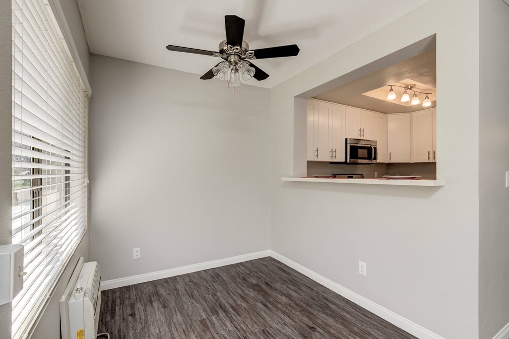an empty living room with a ceiling fan and a kitchen