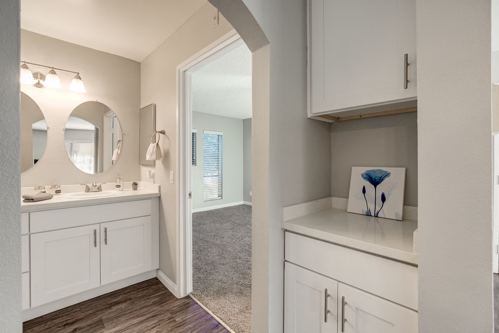 a kitchen with white cabinets and a mirror and a door to a hallway