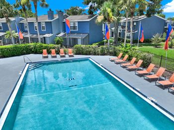 A swimming pool surrounded by orange lounge chairs and blue flags.