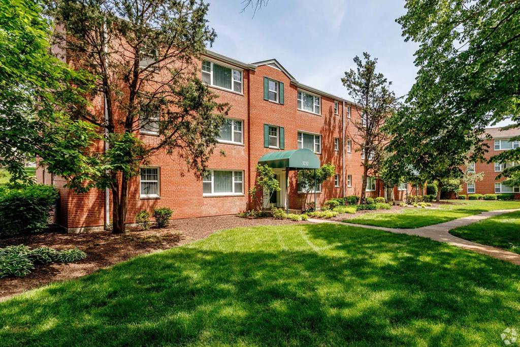 exterior view of a brick apartment building with green grass and trees at Hampton Gardens, Missouri, 63139