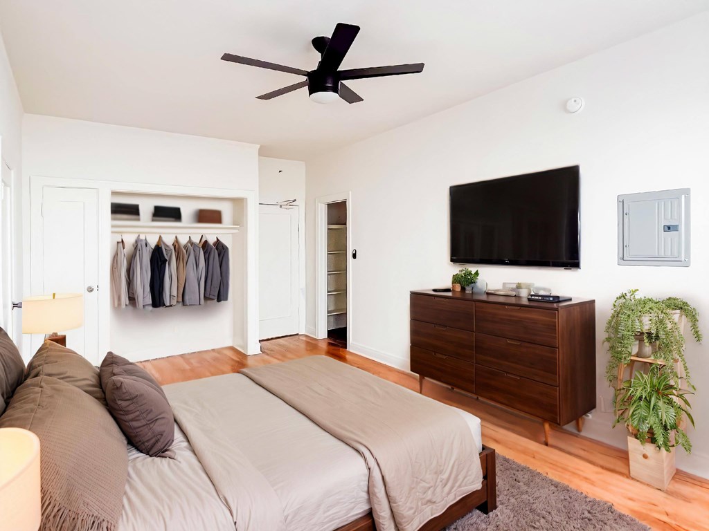 A bedroom with a bed, a ceiling fan, a wardrobe, a TV, and a plant at Kenmore Park Apartments, Los Angeles