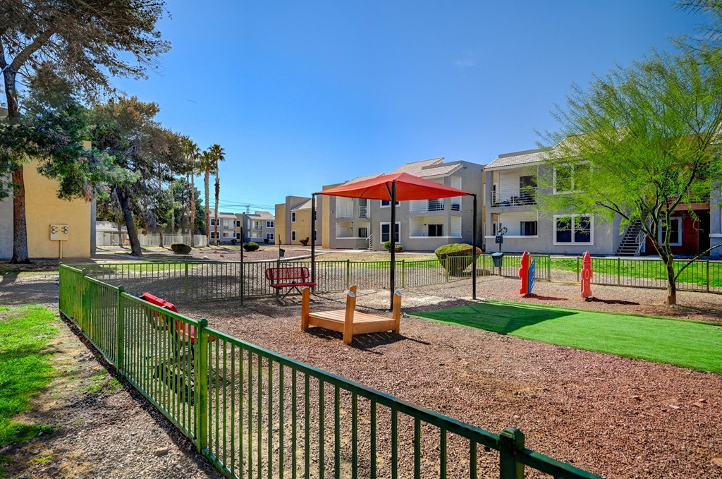 A playground with a green fence and a red umbrella.