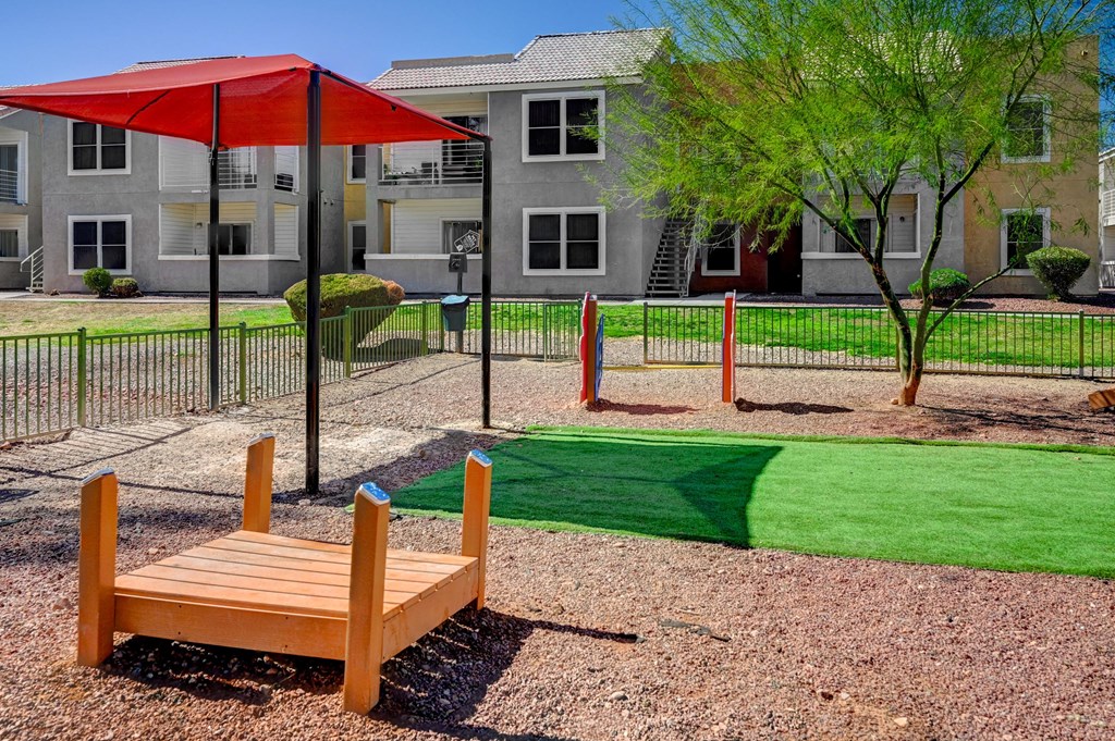 A playground with a red umbrella and a wooden bench.